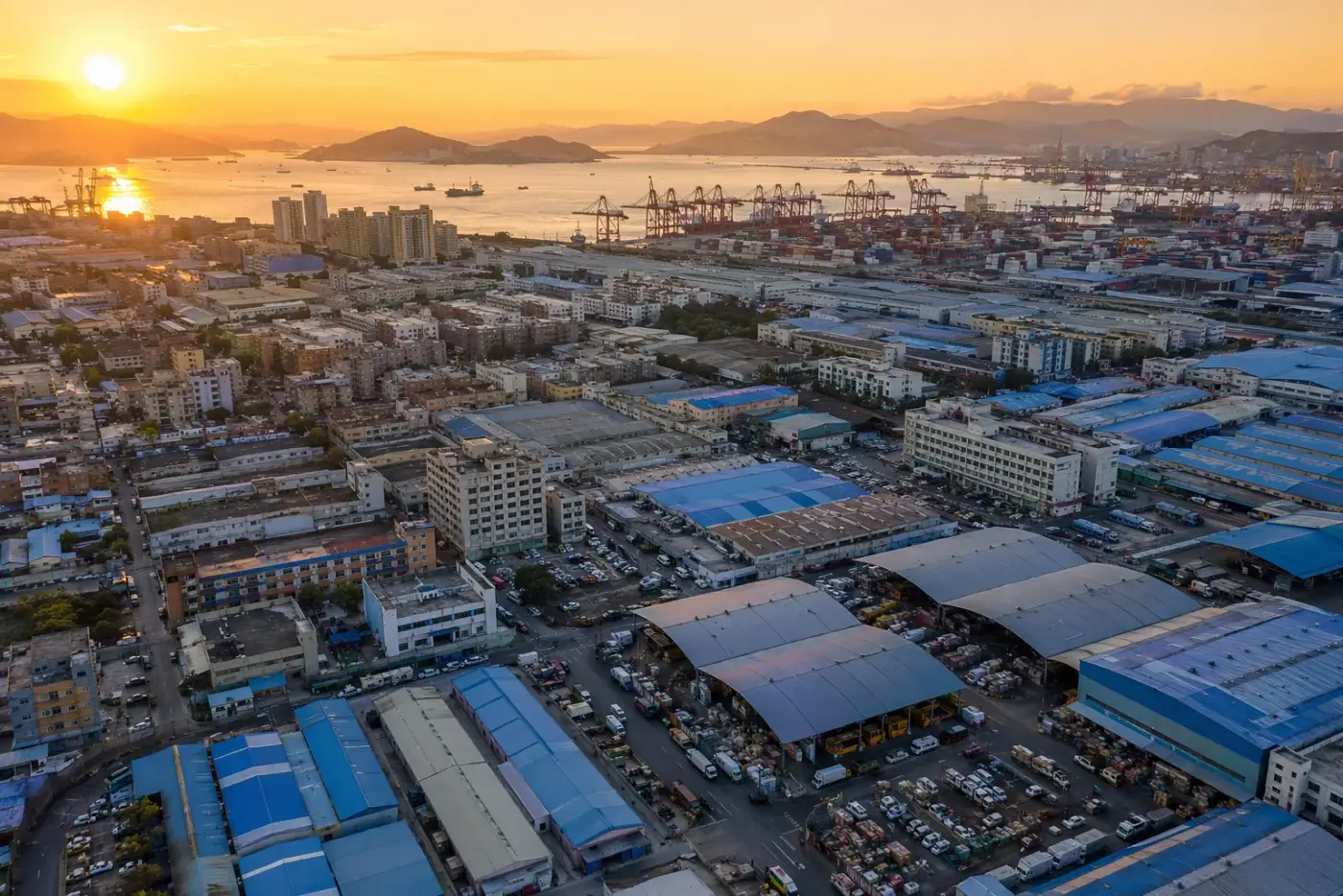 Vista aérea de una ciudad manufacturera china con fábricas, pabellones de mercados mayoristas y un puerto de contenedores al fondo
